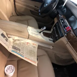 Wnętrze samochodu BMW z beżową skórzaną tapicerką, zabezpieczone gazetami i taśmą malarską podczas renowacji, widoczny pojemnik z preparatem do skóry na siedzeniu pasażera.