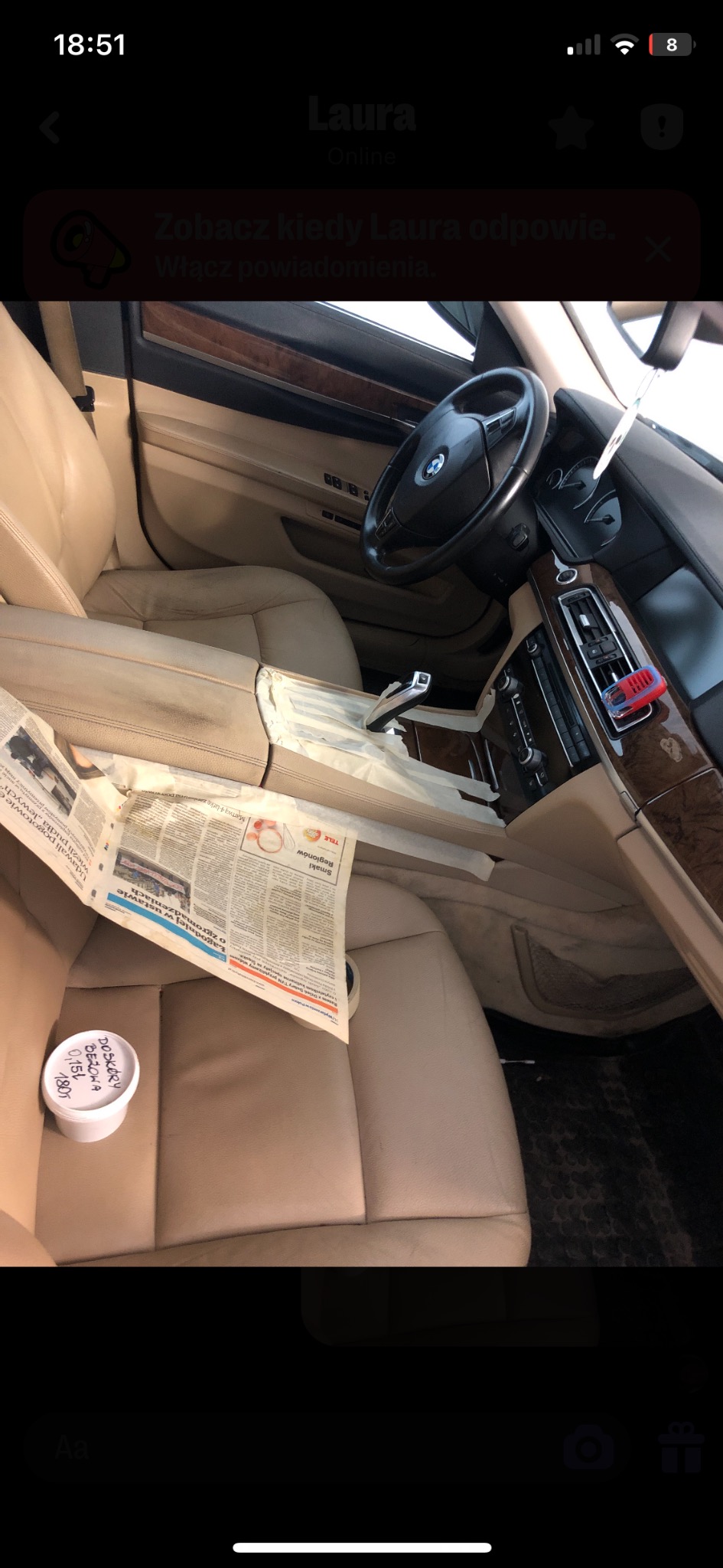 Wnętrze samochodu BMW z beżową skórzaną tapicerką, zabezpieczone gazetami i taśmą malarską podczas renowacji, widoczny pojemnik z preparatem do skóry na siedzeniu pasażera.