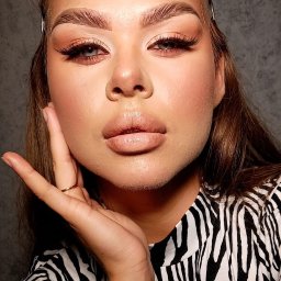 Aleksandra Smętek - Portret kobiety z pełnym makijażem, w bluzce w zebrę, z dłonią przy twarzy, eksponujący makijaż oczu i ust.