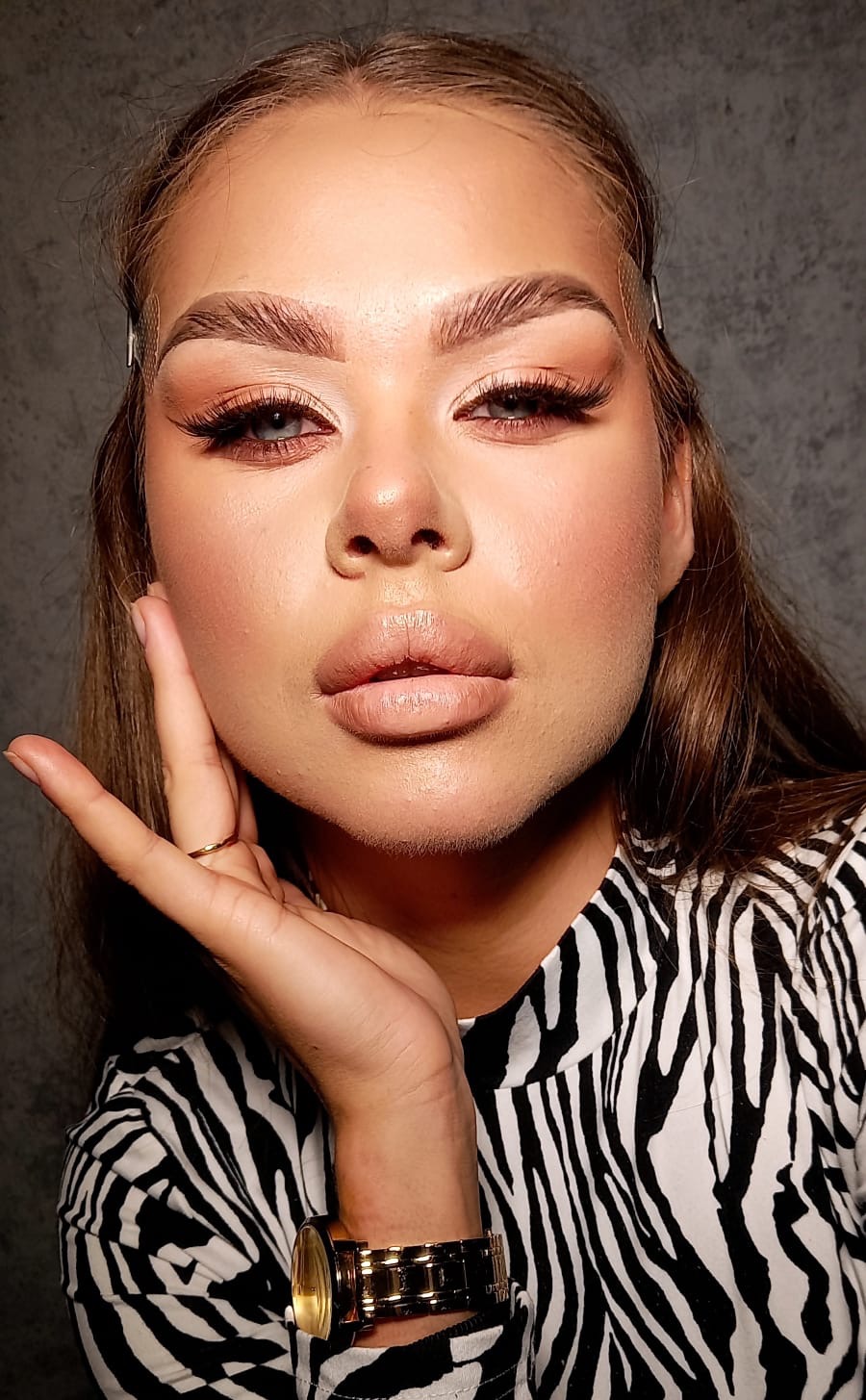 Portret kobiety z pełnym makijażem, w bluzce w zebrę, z dłonią przy twarzy, eksponujący makijaż oczu i ust.