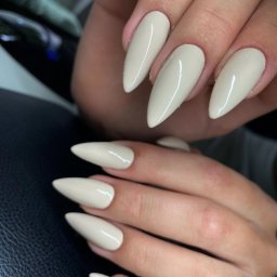 Euforia by Patrycja Frączek - Dłonie z beżowymi, błyszczącymi paznokciami w kształcie szpiców na tle czarnej skórzanej powierzchni.