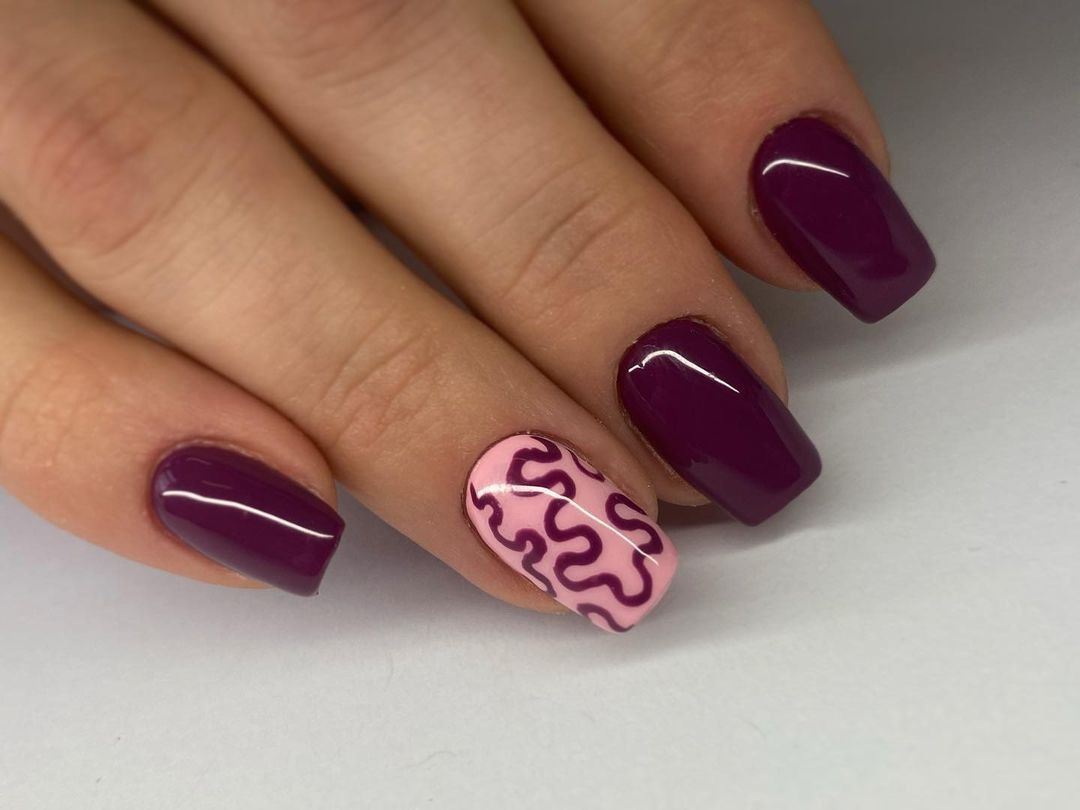 Dłoń z paznokciami pomalowanymi na ciemny fiolet i jasny róż z ciemnofioletowym wzorem wijących się linii.