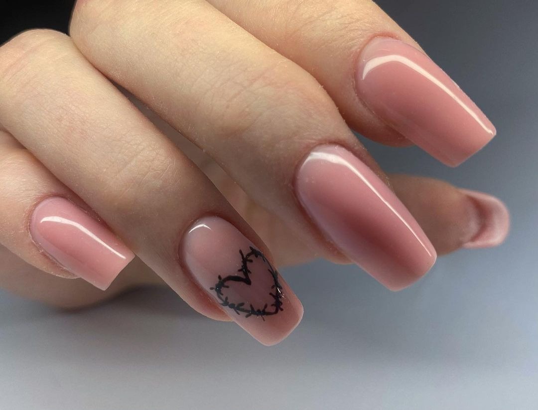 Delikatne, różowe paznokcie o kwadratowym kształcie, jeden z paznokci ozdobiony czarnym rysunkiem serca oplecionego cierniem.