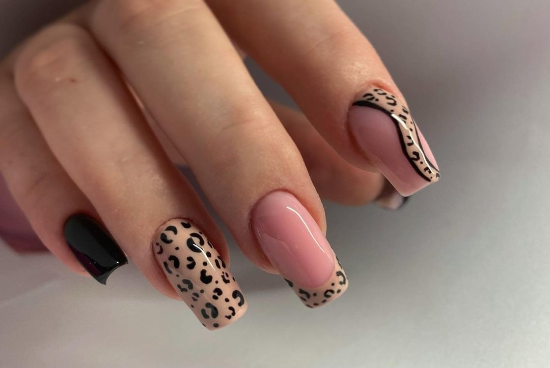 Zbliżenie na dłoń z pomalowanymi paznokciami w różnych stylach: czarny, panterka i różowy french z czarną obwódką.