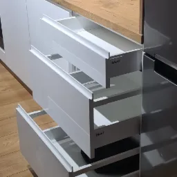 Nowoczesna kuchnia z białymi, wysuwanymi szufladami Blum, drewnianym blatem i czarną armaturą, widok na wnętrze szuflad.