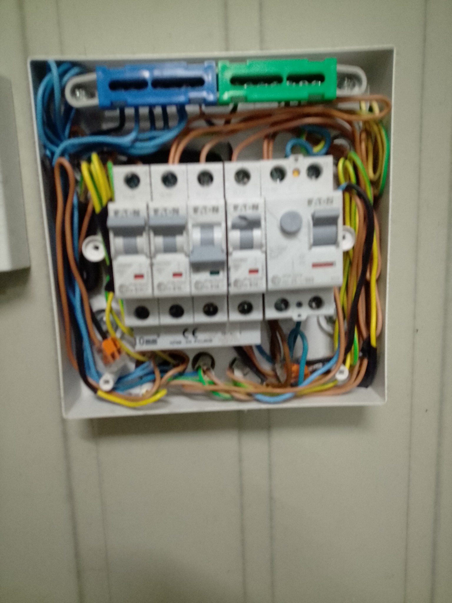 Otwarta skrzynka elektryczna z zamontowanymi bezpiecznikami EATON i kolorowymi przewodami, widoczne złącza WAGO.