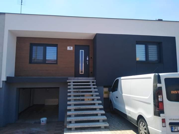 Nowoczesny dom murowany z garażem, elewacją w odcieniach brązu i grafitu, numer domu '13' nad drzwiami, biały samochód dostawczy zaparkowany przed wejściem.