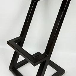 Nowoczesny taboret barowy z drewnianym siedziskiem i geometryczną, spawaną podstawą z metalowych profili w kolorze ciemnego brązu, na białym tle.