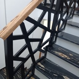 SPAW-MIX PIOTR SĘKTAS - Nowoczesne schody z czarnymi, marmurkowymi stopniami i geometryczną, czarną balustradą z drewnianym pochwytem.