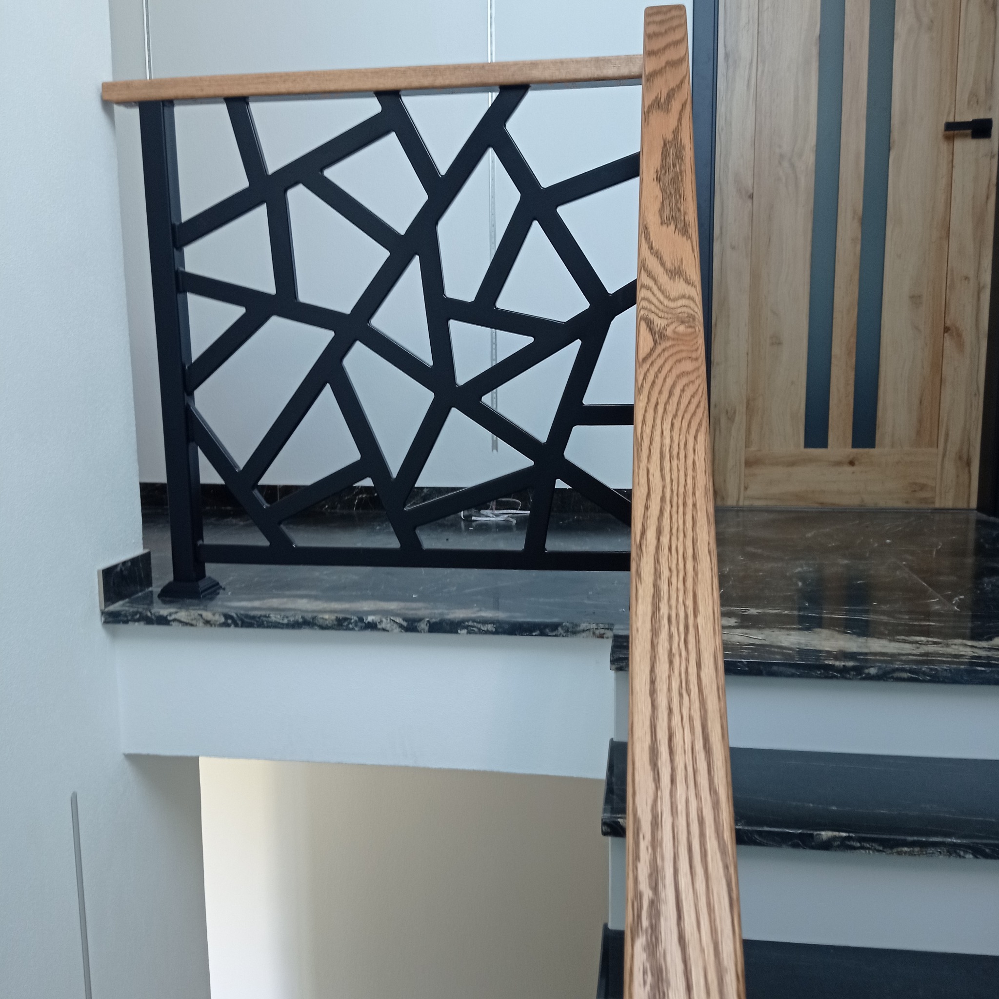 Nowoczesna poręcz schodowa z czarnym metalowym wypełnieniem o geometrycznym wzorze i drewnianym uchwytem, zamontowana na schodach w Wicko.