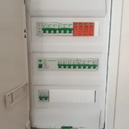 Otwarta, biała skrzynka elektryczna EPN w ścianie, widoczne bezpieczniki i wyłączniki różnicowoprądowe. Minimalistyczny design, wnętrze mieszkania.