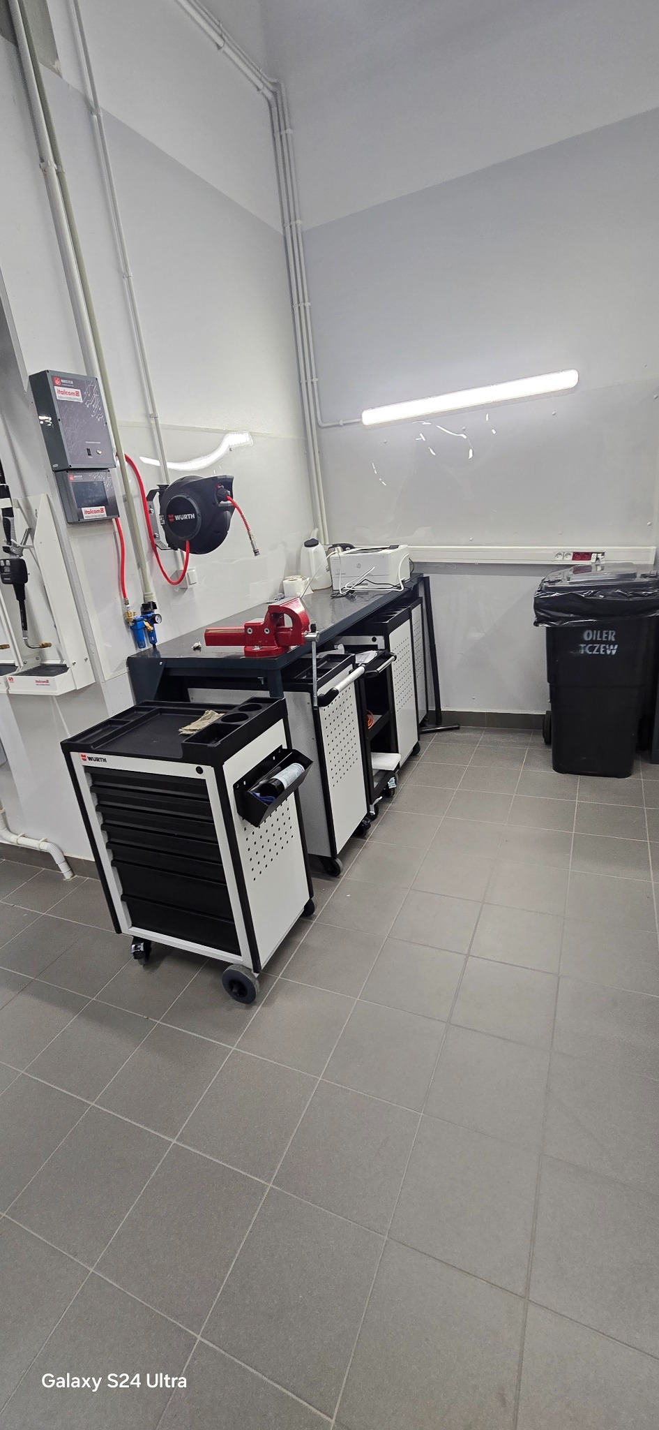 Warsztat elektryczny: stół roboczy z narzędziami Würth, szafki na kółkach, przewody elektryczne na ścianie. Uporządkowana przestrzeń pracy.