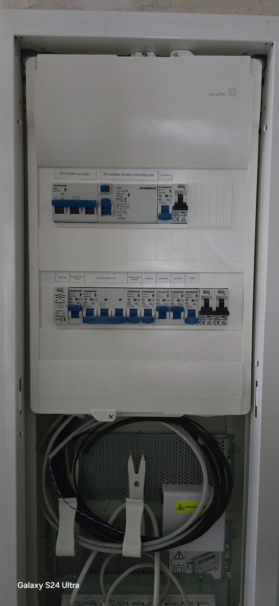 Rozdzielnica elektryczna Hager Volta IP30 z wyłącznikami Schrack i Ideal. Widoczne zabezpieczenia, przewody i oznaczenia obwodów. Całość w białej obudowie.