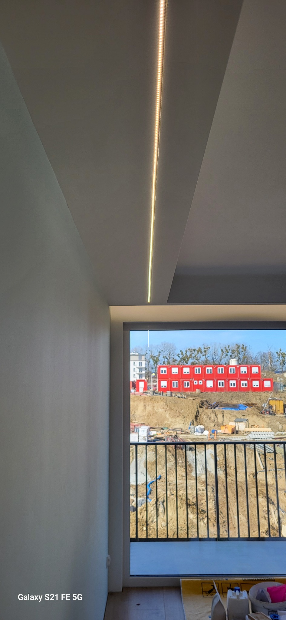 Nowoczesne oświetlenie LED w suficie, listwa świetlna w Kartuzach. Widok z okna na teren budowy.