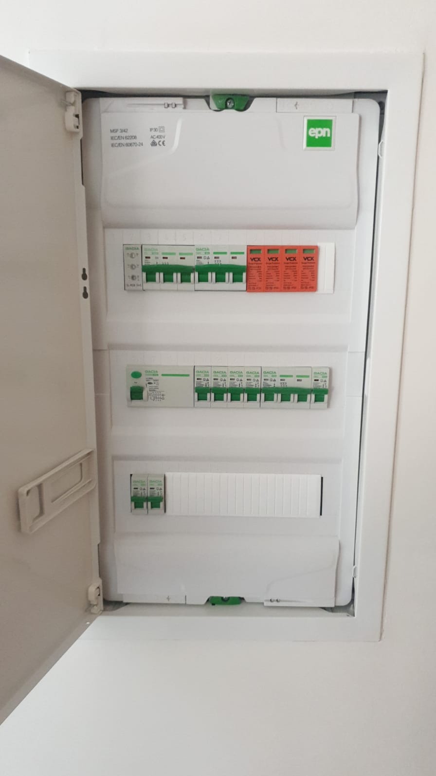 Otwarta, biała skrzynka elektryczna EPN w ścianie, widoczne bezpieczniki i wyłączniki różnicowoprądowe. Minimalistyczny design, wnętrze mieszkania.