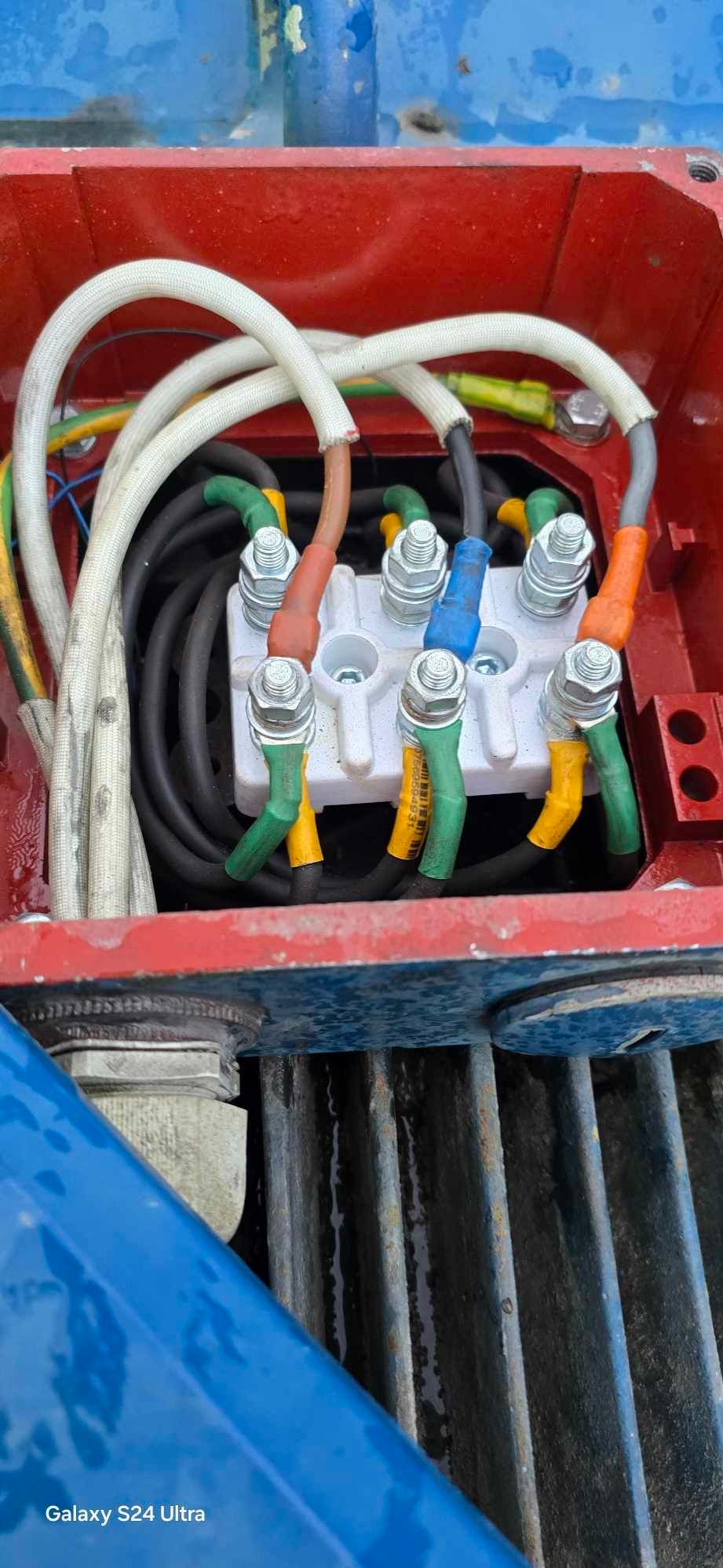 Szczegółowe ujęcie podłączenia przewodów elektrycznych do listwy zaciskowej w czerwonej obudowie, z widocznymi kolorowymi oznaczeniami i śrubami mocującymi.