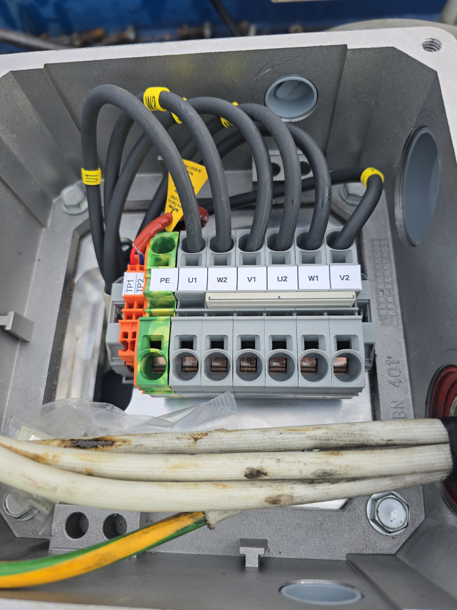 Szare kable z oznaczeniami podłączone do listwy zaciskowej w metalowej skrzynce. Widoczne oznaczenia U1, W2, V1, U2, W1, V2 oraz TP1, TP2 i PE na zaciskach.