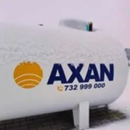 Biały zbiornik z logo AXAN i numerem telefonu, częściowo przysypany śniegiem, stojący na kostce brukowej.