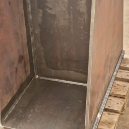 Uslugi Spawalniczo-Monterskie - Surowa, spawana metalowa konstrukcja w kształcie prostopadłościanu bez jednej ściany, umieszczona na drewnianej palecie, widoczne spawy.