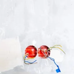 Dwa czerwone, okrągłe puszki elektryczne zamontowane w szarej, surowej ścianie, z wystającymi przewodami w kolorach niebieskim, żółtym i brązowym.