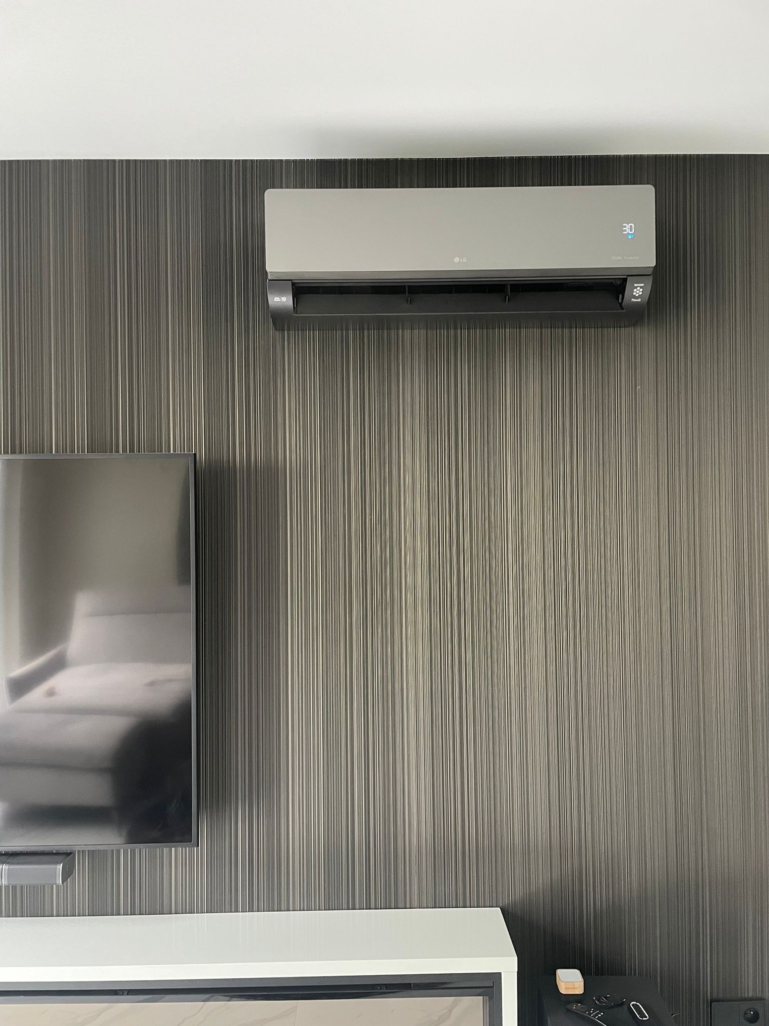 Szary klimatyzator LG Dual Inverter zamontowany na ciemnej, teksturowanej ścianie w salonie w Gdańsku, obok telewizora.
