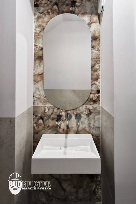 Nowoczesna łazienka z umywalką nablatową i lustrem w kształcie łuku na tle marmurowej ściany. Minimalistyczny design, chromowana armatura, eleganckie wykończenie.