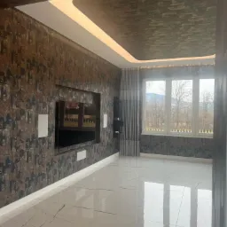 Pokój po remoncie z wzorzystą tapetą na ścianach i suficie, podświetlanym sufitem podwieszanym, dużym oknem z widokiem na góry i błyszczącą, marmurową podłogą.