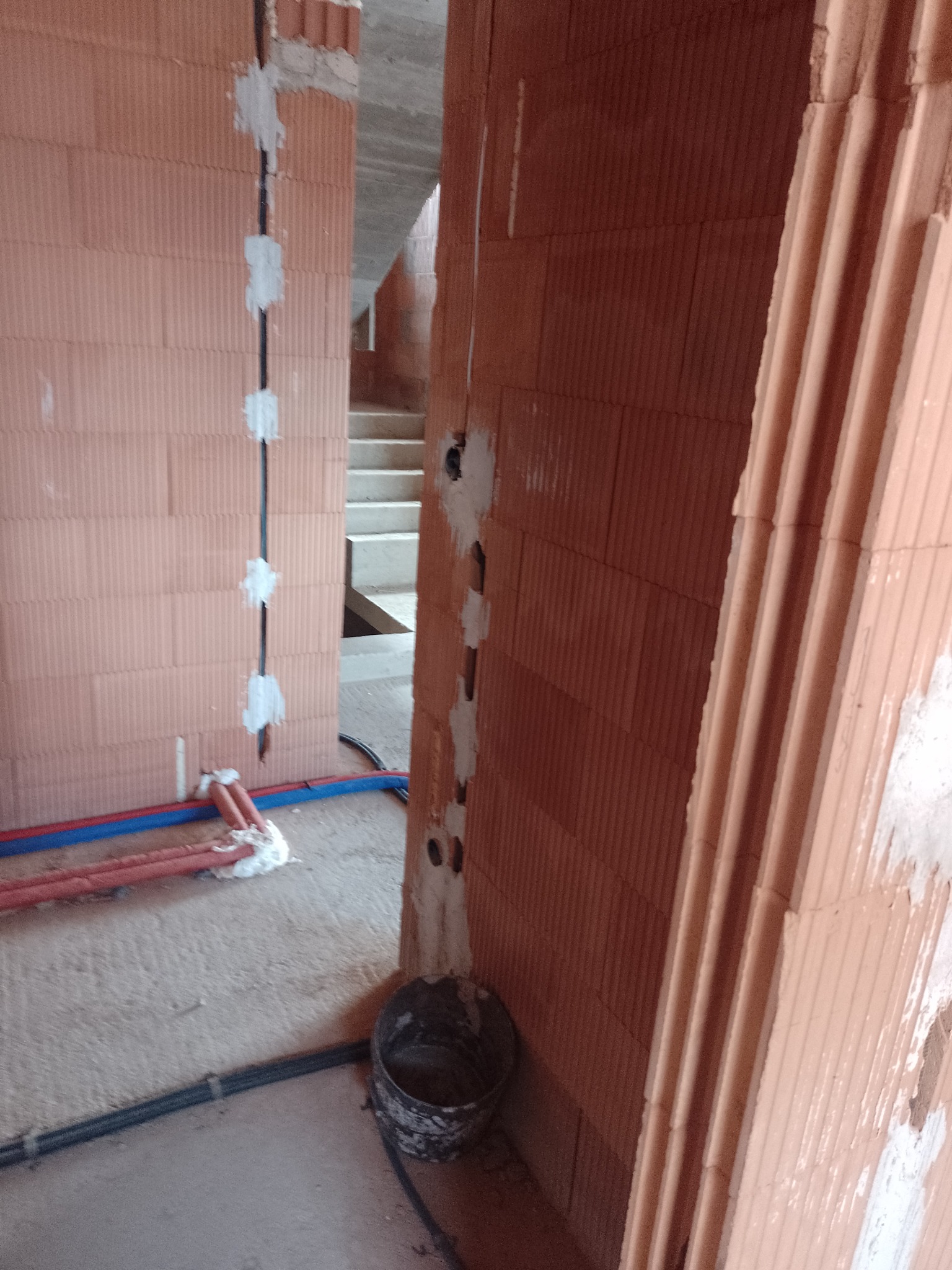 Wewnętrzne ściany z pustaków w surowym stanie w Podwilku, z widocznymi przewodami elektrycznymi zamocowanymi gipsem i rurami instalacji wodnej przy podłodze.