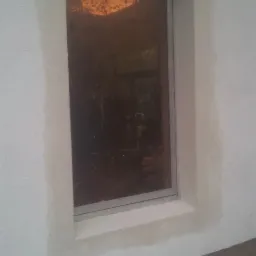 Nowe okno z brązową szybą, osadzone w świeżo otynkowanej ścianie zewnętrznej, widoczne ślady wilgoci na obrzeżach ościeżnicy.