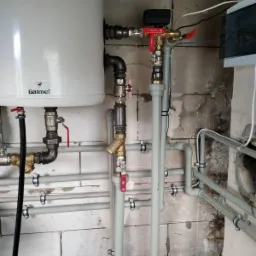 Zamontowany bojler Galmet z licznymi rurami i zaworami w surowym pomieszczeniu z bloczków betonowych.