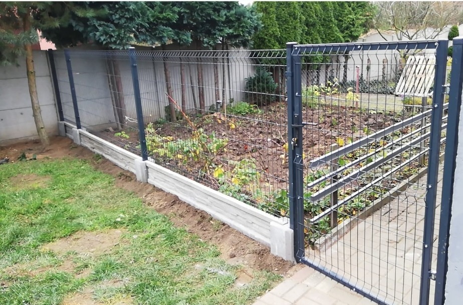 Nowoczesne ogrodzenie panelowe z bramą, osadzone na betonowej podmurówce, widoczne z perspektywy trawnika w ogrodzie.