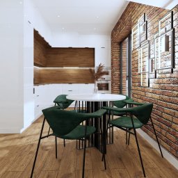 cubeai - projektowanie wnętrz - Wnętrze kuchni z jadalnią: białe szafki z drewnianymi akcentami, okrągły stół z zielonymi krzesłami, ściana z cegły z dekoracjami, drewniana podłoga.