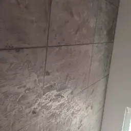 Ściana wykończona płytami imitującymi beton, z widocznymi schodami drewnianymi i fragmentem okna w tle.