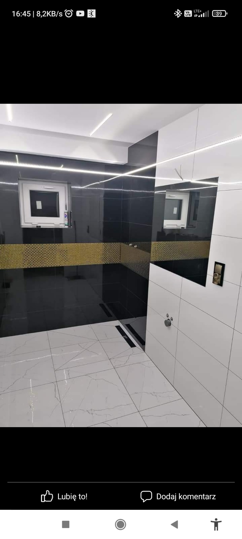 Nowoczesna łazienka z czarno-białymi płytkami, złotym pasem dekoracyjnym, podświetleniem LED i odpływem liniowym w podłodze.