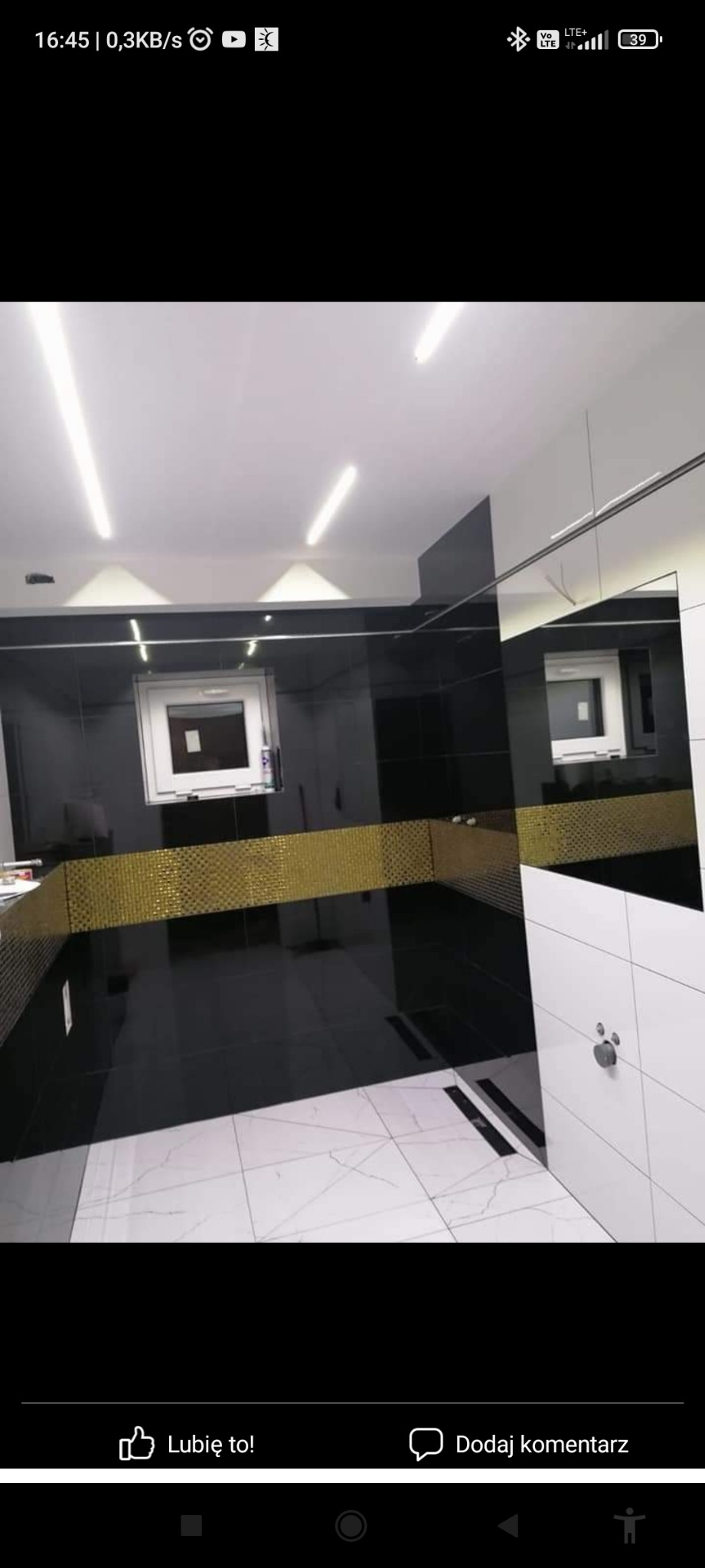 Nowoczesna łazienka z czarnymi płytkami na ścianach, złotym pasem mozaiki i białymi płytkami na podłodze, oświetlona listwami LED.