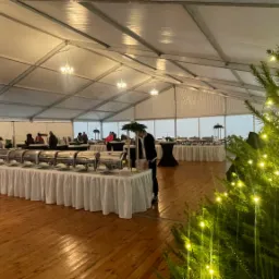 Udekorowany namiot z drewnianą podłogą w Szamotułach, przygotowany do obsługi gości, z bufetem i oświetloną choinką w tle.