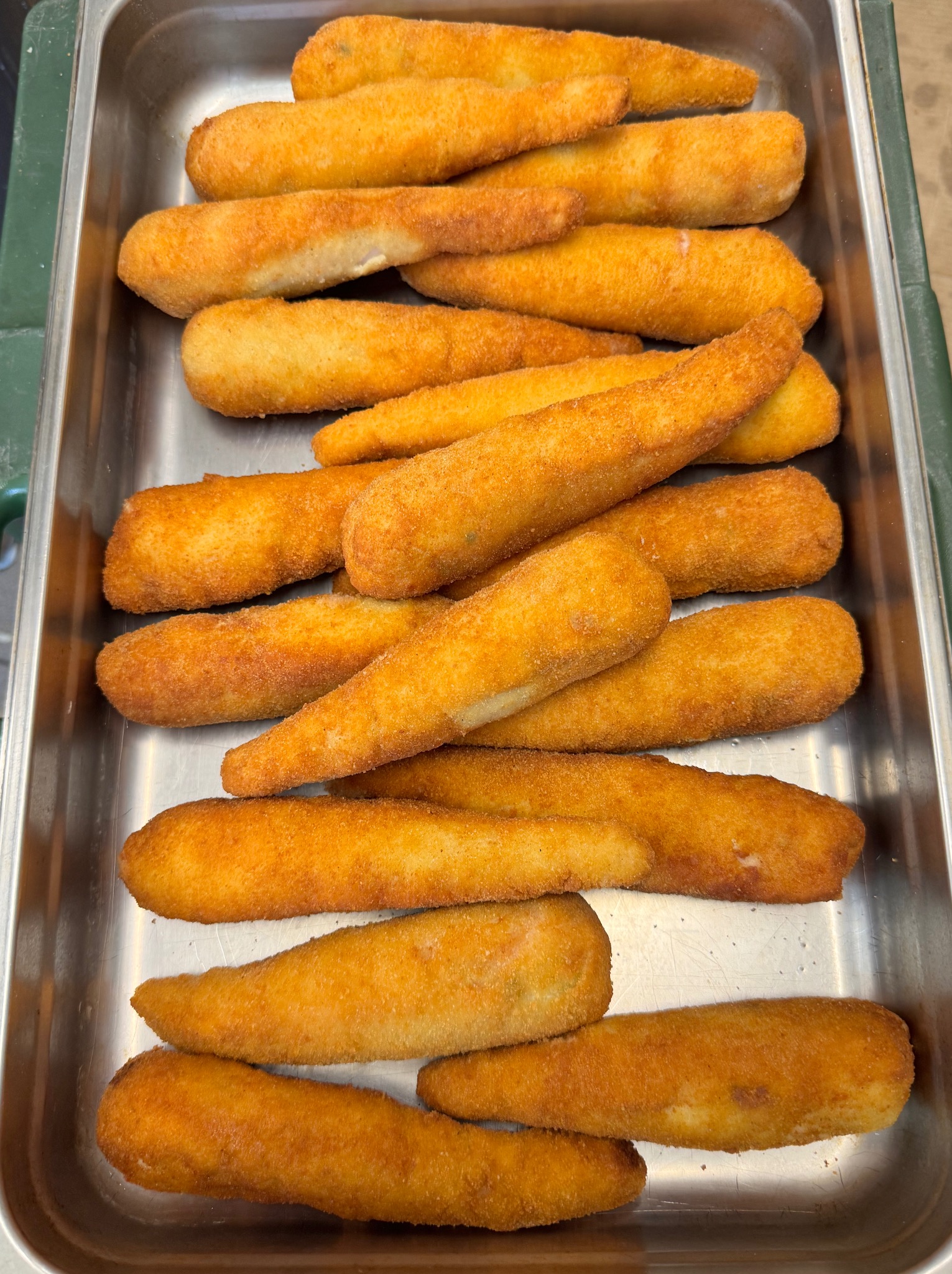 Smażone krokiety w srebrnej, metalowej tacy cateringowej, ułożone warstwami. Złocista panierka, widoczne nierówności i detale tekstury. Przygotowane do serwowania.