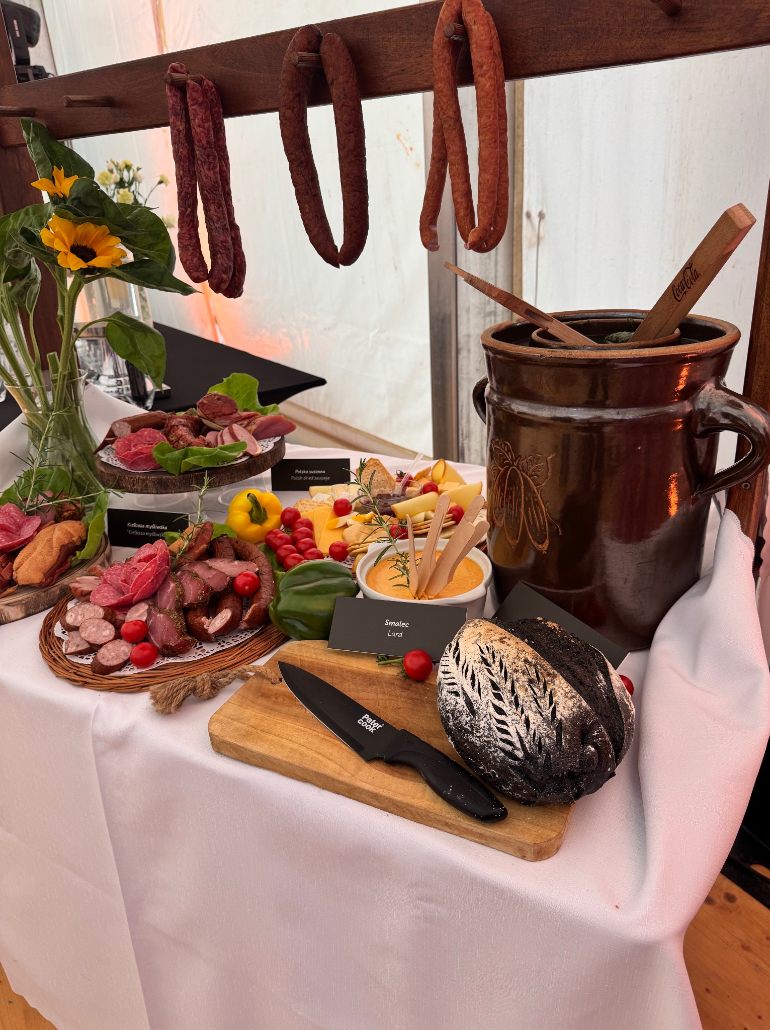 Stół z przekąskami: wędliny, sery, chleb i smalec. Dekoracja z kwiatów słonecznika. Wiejski stół z drewnianymi elementami. Aranżacja cateringu na przyjęcie.