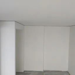 Wnętrze pokoju po malowaniu ścian na biało z szarą listwą przysufitową, widoczne zabezpieczenie podłogi folią malarską.