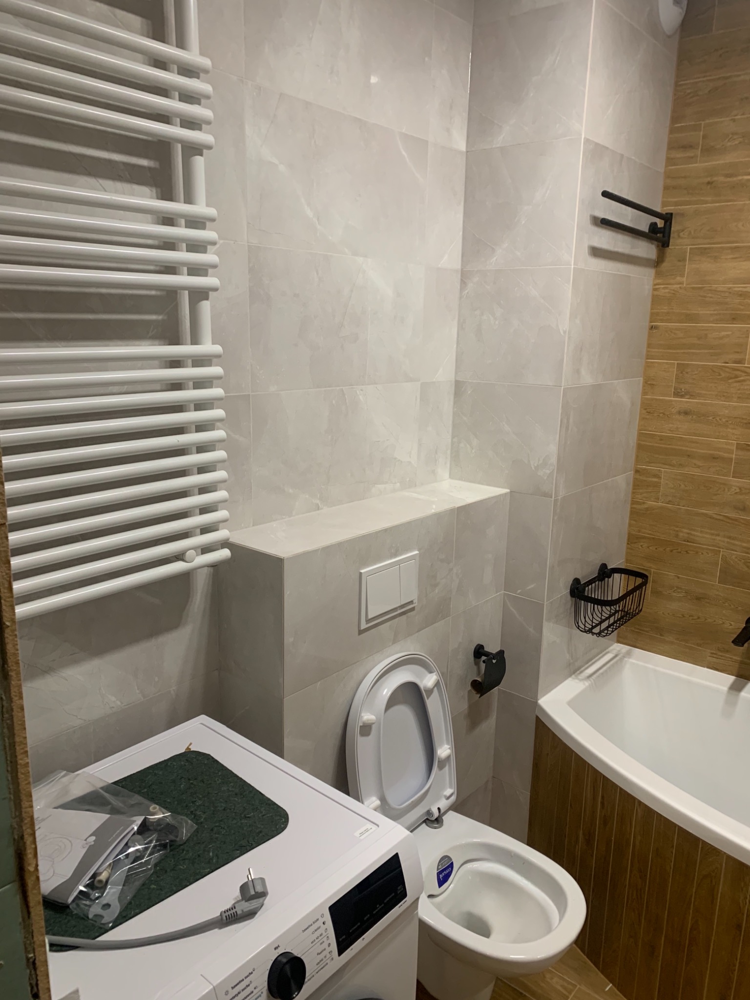 Wykończona łazienka z marmurowymi płytkami, wiszącą toaletą, grzejnikiem drabinkowym i pralką z akcesoriami na wierzchu, widok z niskiego kąta.