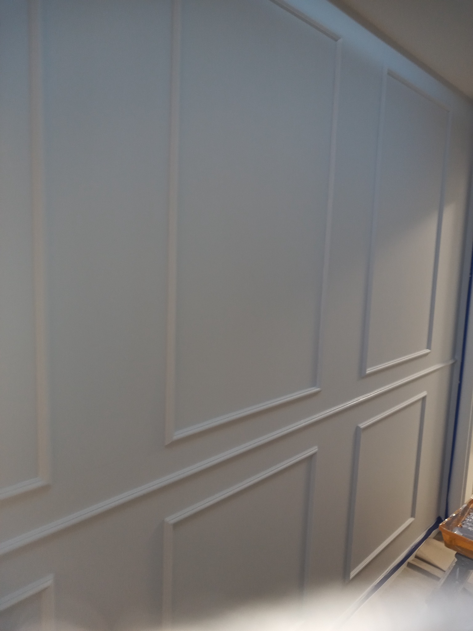 Ściana z dekoracyjnymi panelami ściennymi w odcieniach bieli, widoczne listwy i proste geometryczne wzory, delikatne światło podkreśla strukturę.