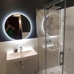 GROSS-CHEF PATRYCJA ŁABSZ - Nowoczesna łazienka z kabiną prysznicową typu walk-in, okrągłym lustrem z podświetleniem LED, wiszącą umywalką z miseczką na mydło i wzorzystą podłogą w odcieniach szarości.