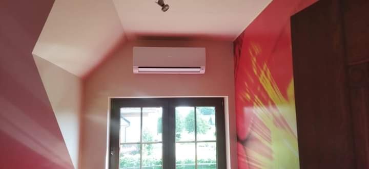 Zamontowany klimatyzator ścienny w pomieszczeniu z oknem i kolorową tapetą, widoczny z niskiego kąta.