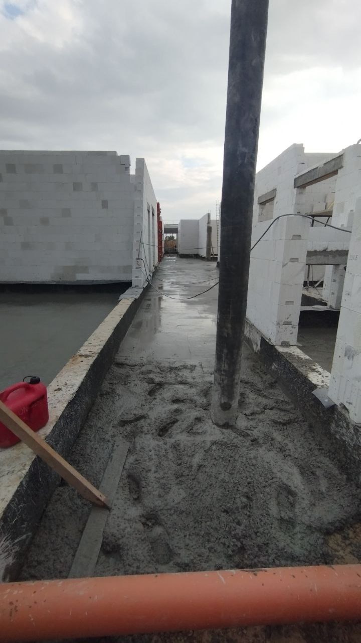 Wylewanie betonu na strop budynku z bloczków betonu komórkowego, widoczny przewód pompy do betonu i ślady butów w świeżym betonie.