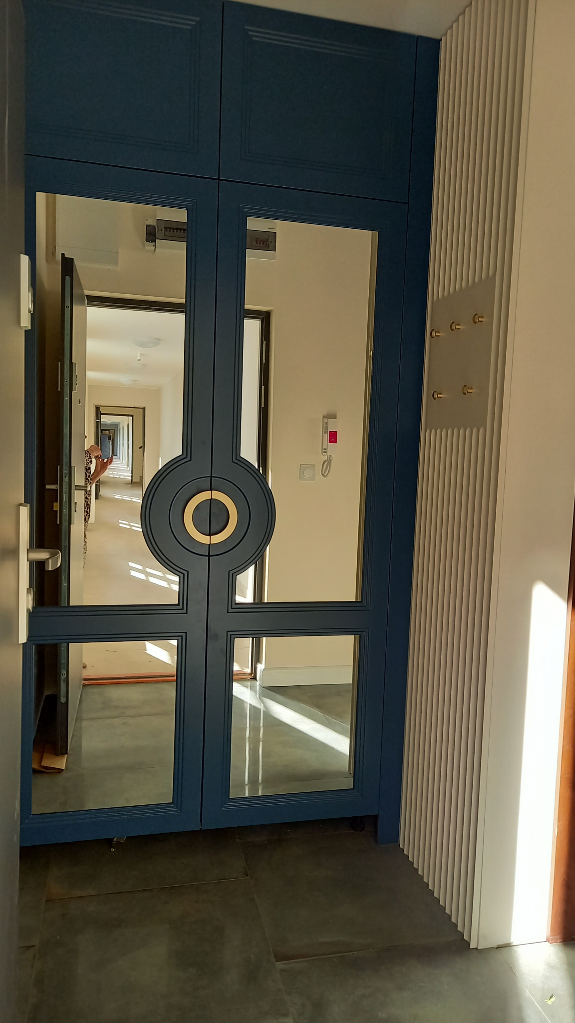 Nowoczesne, dwuskrzydłowe drzwi wewnętrzne w kolorze granatowym z geometrycznym, okrągłym zdobieniem w kolorze złota, wpuszczone w ścianę z dekoracyjnymi listwami pionowymi i wieszakami na ubrania,...