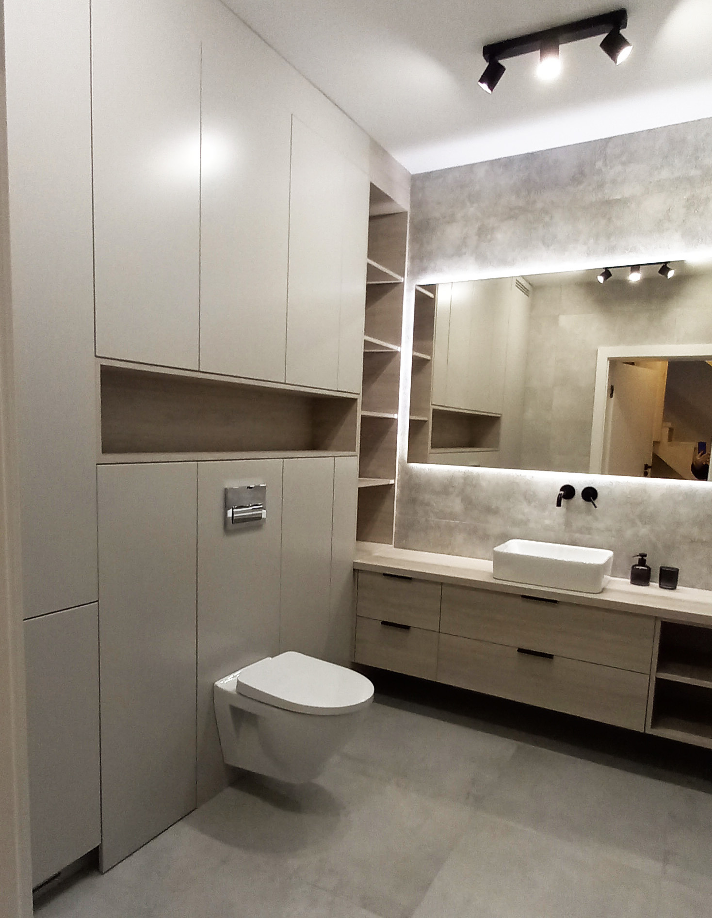 Nowoczesna łazienka z zabudową meblową w odcieniach beżu, wisząca toaleta, umywalka nablatowa i lustro z podświetleniem LED.