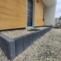 Wykończona obrzeżem z ciemnej kostki rabata z jasnym żwirem przy domu w Sosnowcu, widok z niskiej perspektywy.