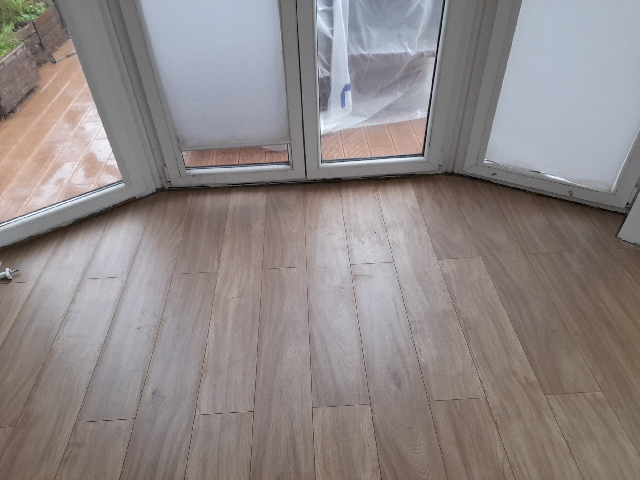 Ułożone panele podłogowe w pokoju z oknem balkonowym, widoczne zabezpieczenie folią malarską na oknach.