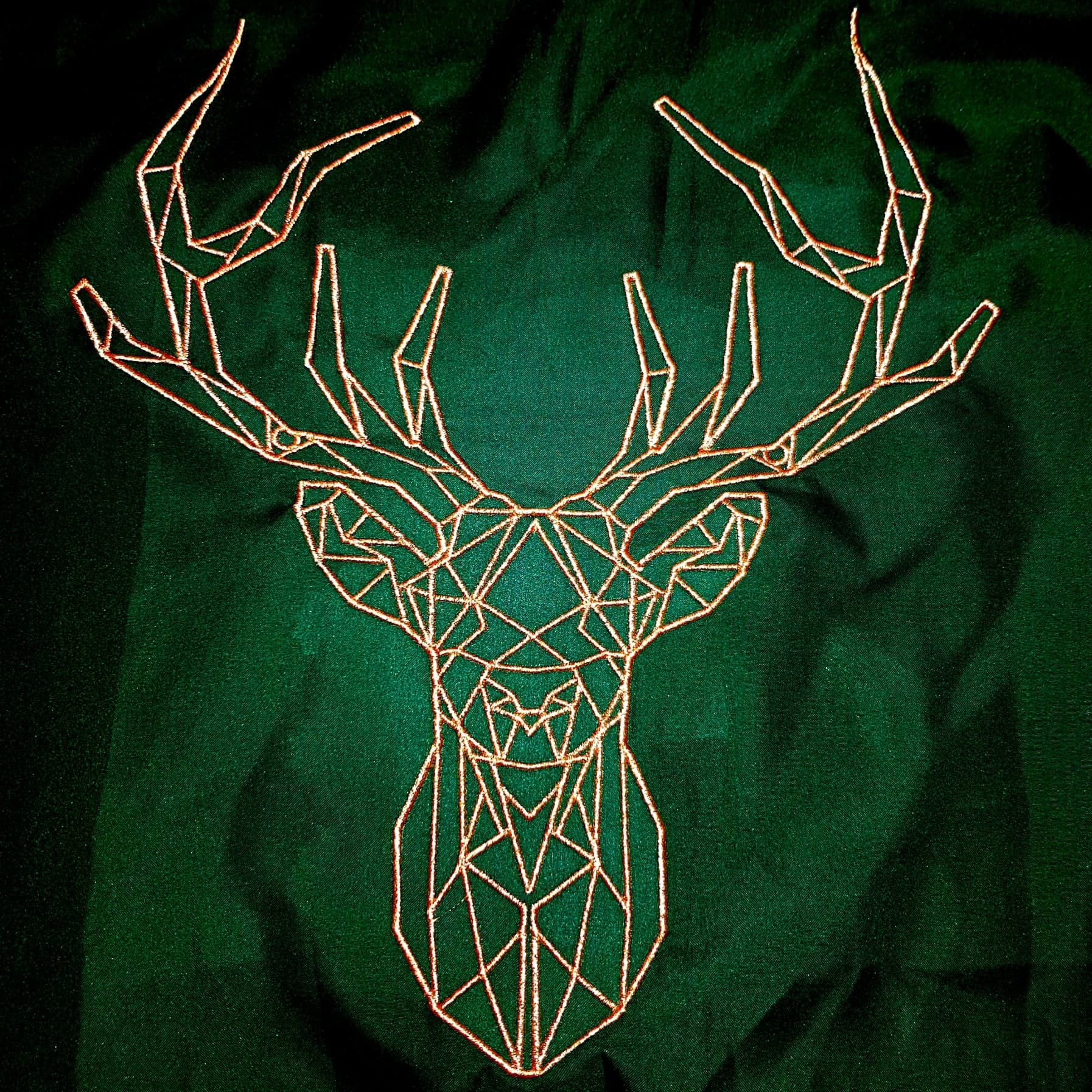 Geometryczny haft głowy jelenia w odcieniach brązu na ciemnozielonej tkaninie.