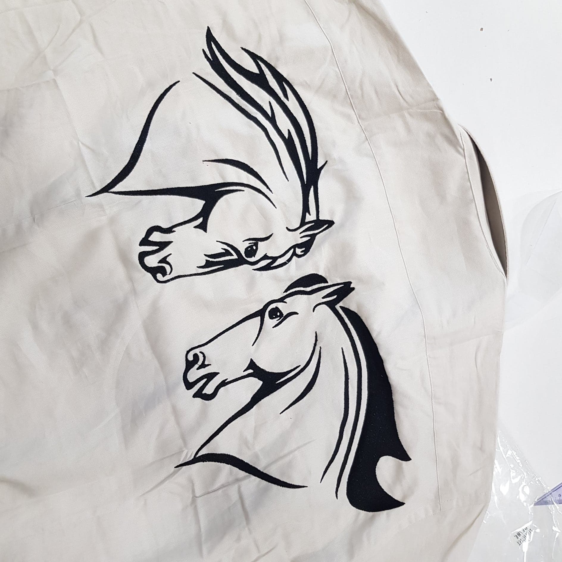 Beżowa kamizelka z wyhaftowanymi czarnymi konturami głowy konia i fantazyjnego ptaka.